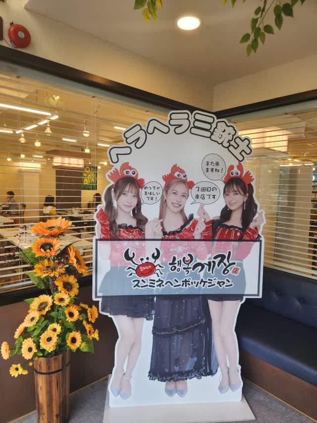 홀 한쪽에 세워진 브랜드 포토 스탠디와 해바라기 화병, 뒤로 보이는 창가 좌석